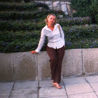 Woman stands near a wall and car in a garden.