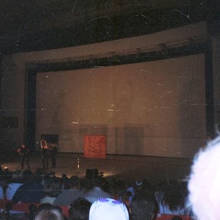 Audience viewing a stage with a screen and speaker.
