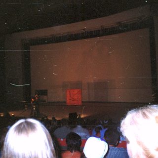 Audience seated, facing a stage with a screen.