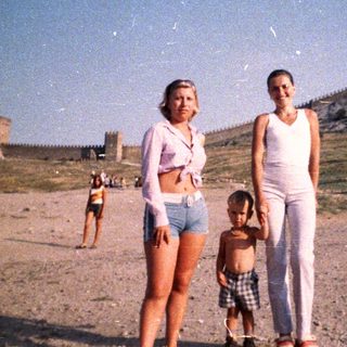 Two women and a child stand near a fortress.