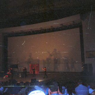 Concert stage with performers, audience visible in background.