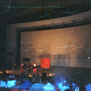 Performers on stage with audience visible in a theater.