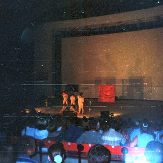 Stage performance with audience visible in darkened theater.