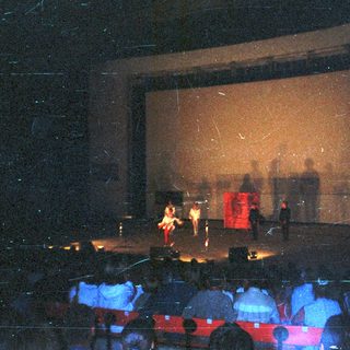 Stage performance with performers and audience in dim lighting.