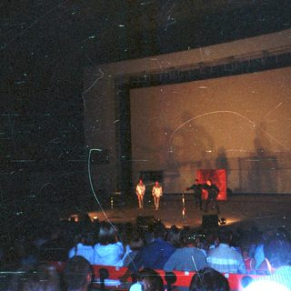 Performers on stage during a show with audience seated.