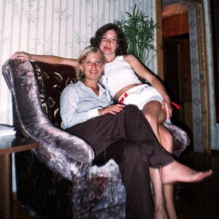 Two women sit in a chair in a patterned room.