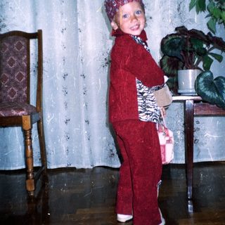Child in red suit stands near plants, indoors.