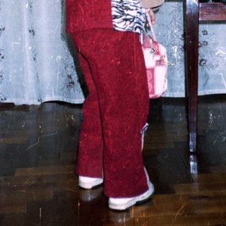 Child in red suit stands near plants, indoors.