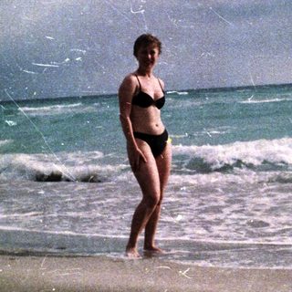Woman stands on a beach with waves in the background.