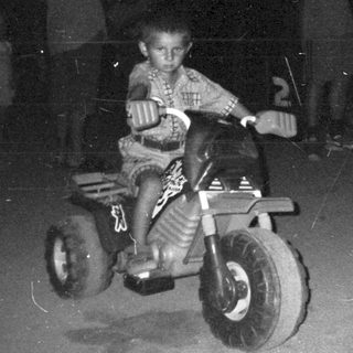 Boy riding a tricycle at night with onlookers.