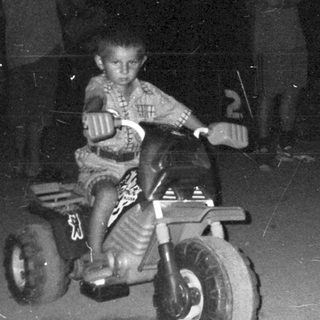 Boy riding a tricycle at night with onlookers.