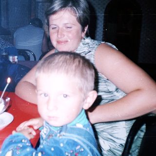 Boy sits on a lap, eating dessert with family.