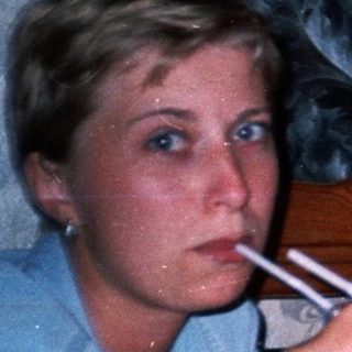 Couple sits at a table, one smoking, background visible.