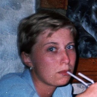 Couple sits at a table, one smoking, background visible.
