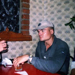 Couple sits at a table, one smoking, background visible.