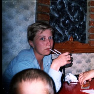 Couple sits at a table, one smoking, background visible.
