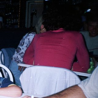 Boy sleeps on table with drinks and people nearby.