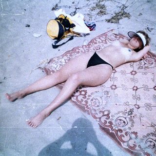 Here's a brief summary of the image: Woman sunbathing on a patterned rug outdoors.