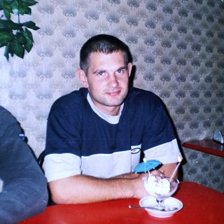 Man sits at a table with dessert, in a patterned room.