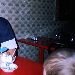 Man sits at a table with dessert, in a patterned room.