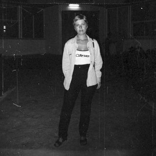 Woman stands in darkness, wearing Versace tank top and blazer.