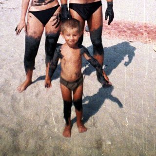 Family covered in dark mud stands on a beach.