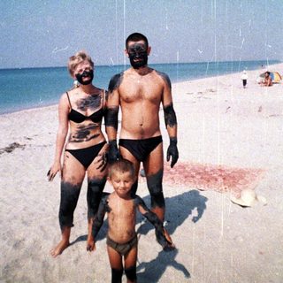 Family covered in dark mud stands on a beach.