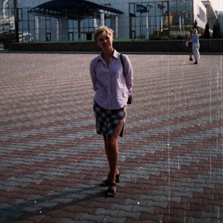 Woman stands in plaza with a large building in background.
