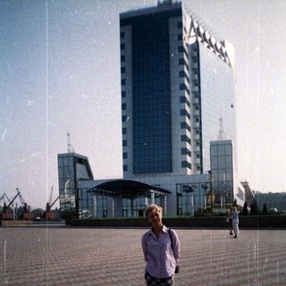 Woman stands in plaza with a large building in background.