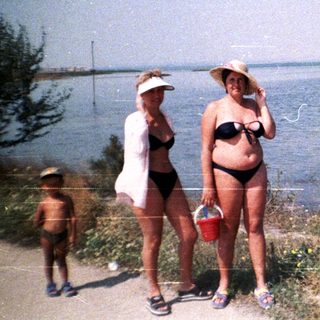 Three people stand near a body of water on a sunny day.