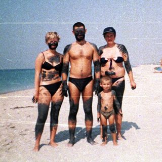 Family covered in dark material stands on a sandy beach.