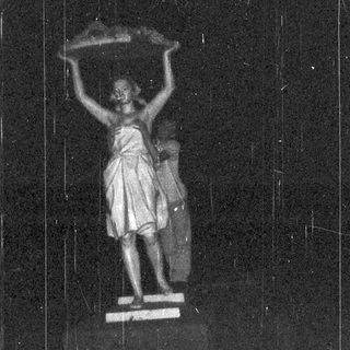 Statue of a woman holding a lamp stands illuminated.