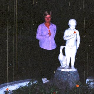 Woman stands near a statue in a garden at night.
