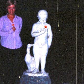 Woman stands near a statue in a garden at night.