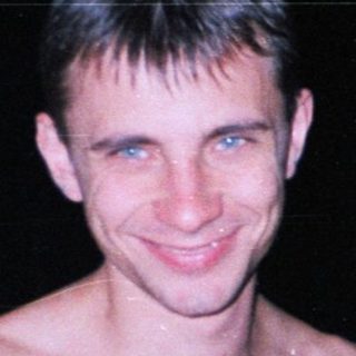 Man with chest hair stands near a railing at night.