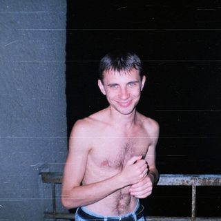 Man with chest hair stands near a railing at night.
