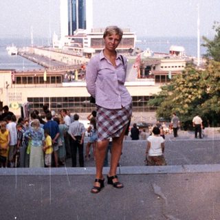 Man stands on steps overlooking a waterfront building and crowd.