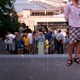Man stands on steps overlooking a waterfront building and crowd.