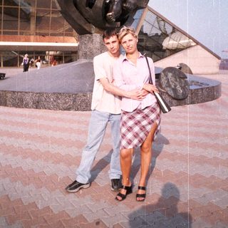 Couple poses near a statue and building outdoors.