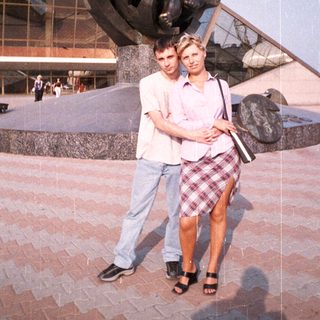 Couple poses near a statue and building outdoors.