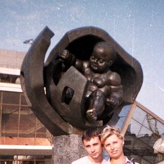 Couple poses near a statue and building outdoors.