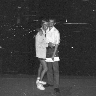 Couple posing outdoors at night, with a cityscape backdrop.
