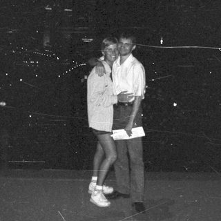 Couple posing outdoors at night, with a cityscape backdrop.