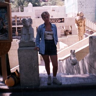 Woman stands near statues and architectural elements outdoors.