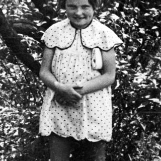 Girl stands in foliage, photographed in black and white.