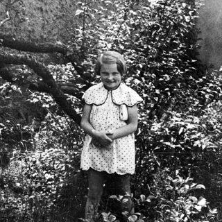 Girl stands in foliage, photographed in black and white.