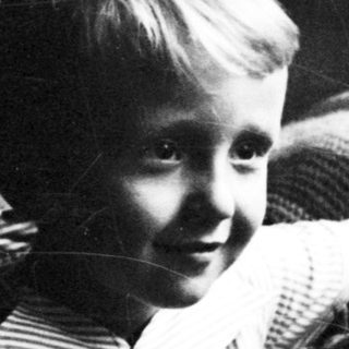 Here's a brief summary: Young boy seated on a patterned armchair, looking toward the viewer.