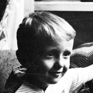 Here's a brief summary: Young boy seated on a patterned armchair, looking toward the viewer.