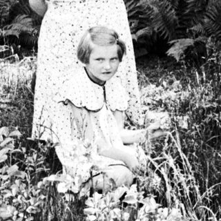 Woman and child stand in a garden, foliage visible.