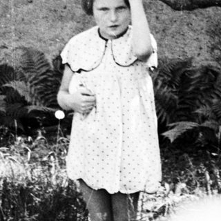 Young girl stands outdoors, holding a tree branch.